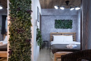 A modern bedroom with a large bed, a wooden headboard, a wall-mounted plant, and a small stool. - CLASSE CINQ (Sapporo)