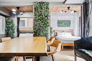 A modern room with a wooden dining table, a bed with a wooden headboard, and a large vertical plant wall. - CLASSE CINQ (Sapporo)