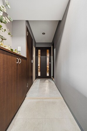 A hallway with a wooden cabinet, a door with a vertical window, and a tiled floor. - CLASSE CINQ (Sapporo)