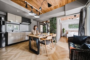Una cocina moderna con comedor, piso de madera, y una sala de estar con sofá y planta.