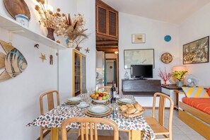 A dining area with a table set for four, a television, and a sofa in the background.