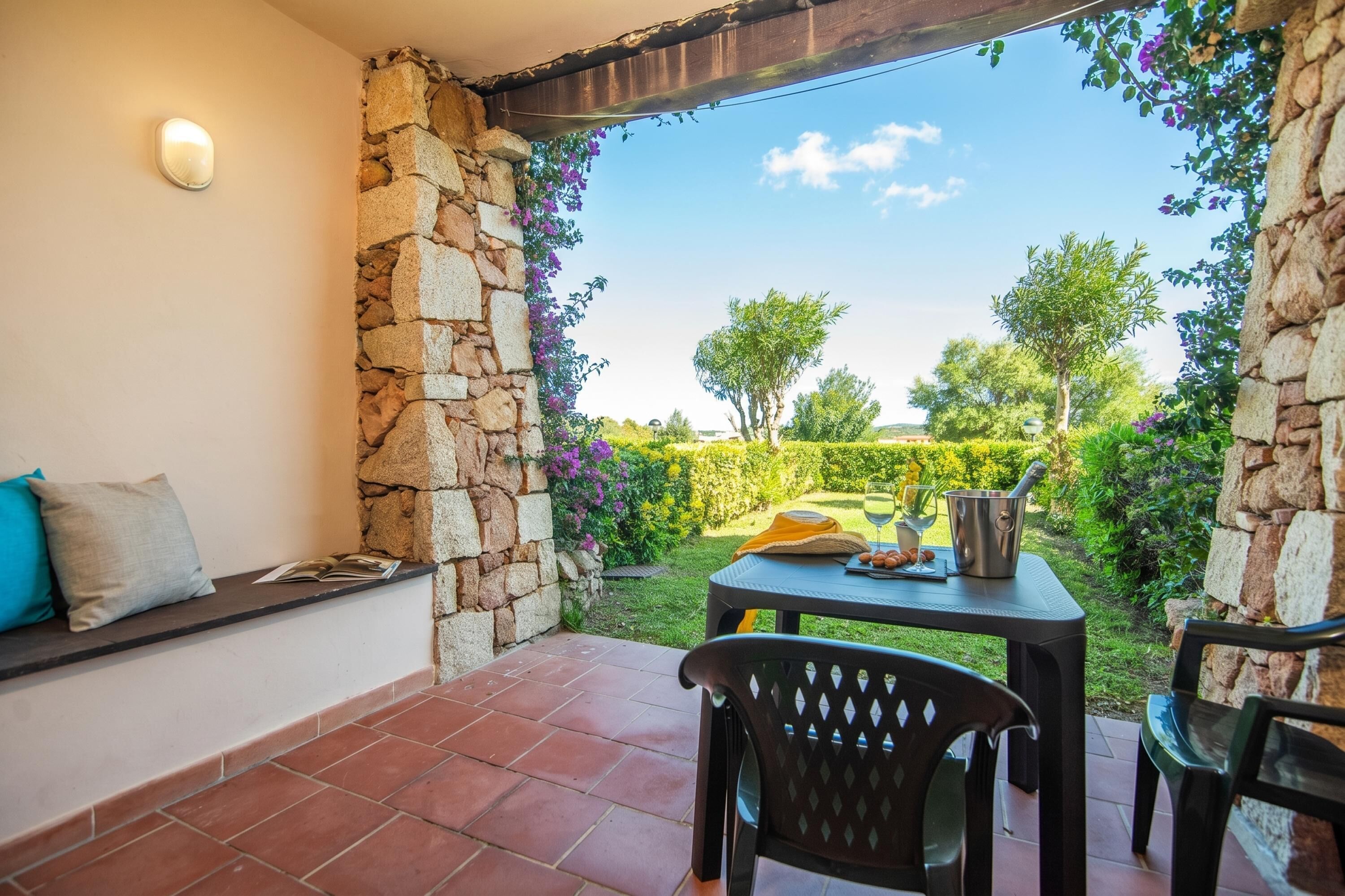 Une terrasse avec des murs en pierre, une table avec des chaises et une vue sur un jardin.