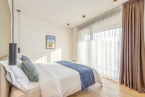 Un dormitorio con cama, mesita de noche, lámpara, ventana con cortinas y un cuadro colgado en la pared.
