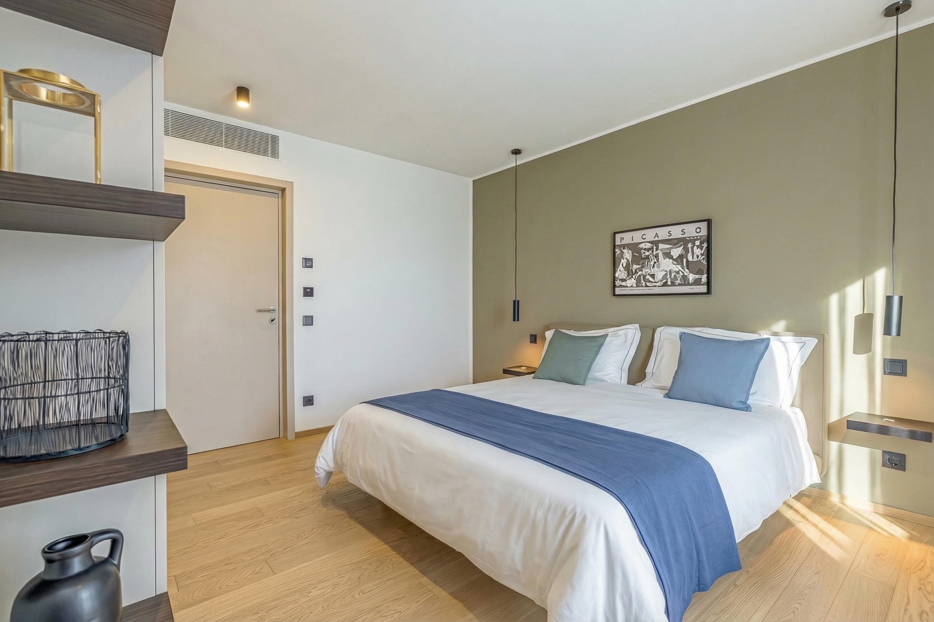 Quarto moderno com uma cama, mesas de cabeceira, uma obra de arte na parede e uma porta.