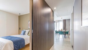 A hotel room with a bed, a wooden partition, a dining area with chairs and a table, and a view of the outside. - ICON H Lugano 602 Suite Executive, Lugano, Switzerland (Lugano)