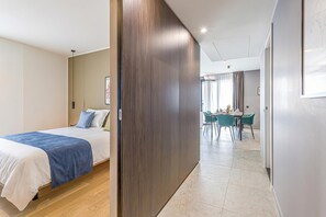 Habitación de hotel con cama, separador de madera, zona de comedor con sillas y una mesa, y vistas al exterior.
