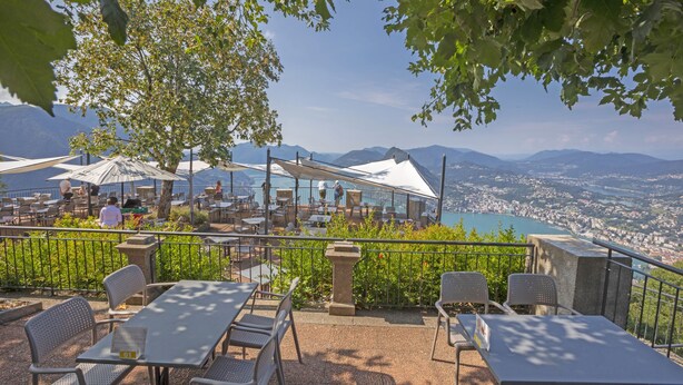 An outdoor terrace with tables and chairs, overlooking a city and mountains. - ICON H Lugano 602 Suite Executive, Lugano, Switzerland (Lugano)