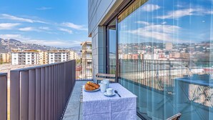 A balcony with a table set for breakfast, a view of the cityscape, and a modern building facade.