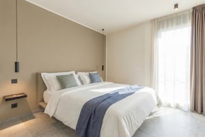 Una habitación de hotel moderna con una cama grande, mesitas de noche, una lámpara colgante y una ventana con cortinas.
