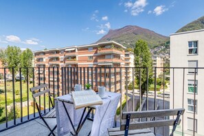 Un balcó amb taula, cadires i un llibre, amb vista a una zona residencial i una muntanya al fons.