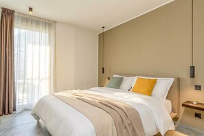 Una habitació d'hotel moderna amb un llit gran, una taula de nit i una finestra amb cortines.