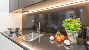 Cozinha moderna com eletrodomésticos de aço inoxidável, pia e bancada com legumes frescos e uma planta em vaso.