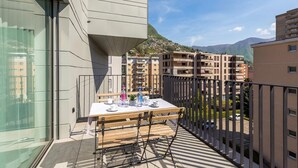 En balkon med et spisebord, udsigt til boligbygninger og et bjerg i baggrunden.