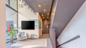 Un intérieur moderne avec un escalier, un téléviseur à écran plat fixé au mur, une plante en pot et un canapé de couleur claire.