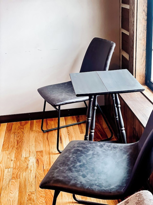 A corner of a room with two black metal chairs and a small table. The floor is wooden, and there is a wooden wall panel on the right.
