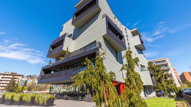 Un immeuble moderne à plusieurs étages, doté de balcons, d’un toit plat et surplombant un ciel dégagé.