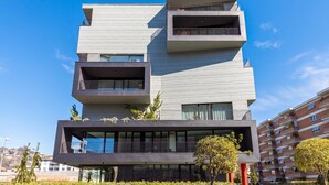 A modern multi-story building with balconies, large windows, and a flat roof.