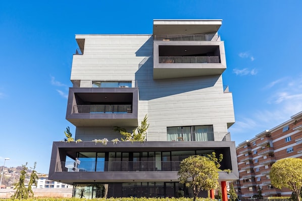 A modern multi-story building with balconies, large windows, and a flat roof.