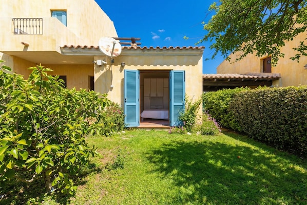 A small house with a garden, a satellite dish, and a door with shutters.