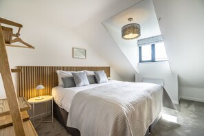 Une chambre avec un plafond en pente, un lit avec une tête de lit, une table de chevet avec une lampe et un luminaire suspendu.