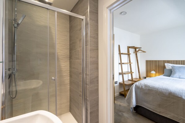 Ein modernes Badezimmer mit Duschkabine aus Glas, einer weißen Badewanne und einer Holzleiter an der Wand.
