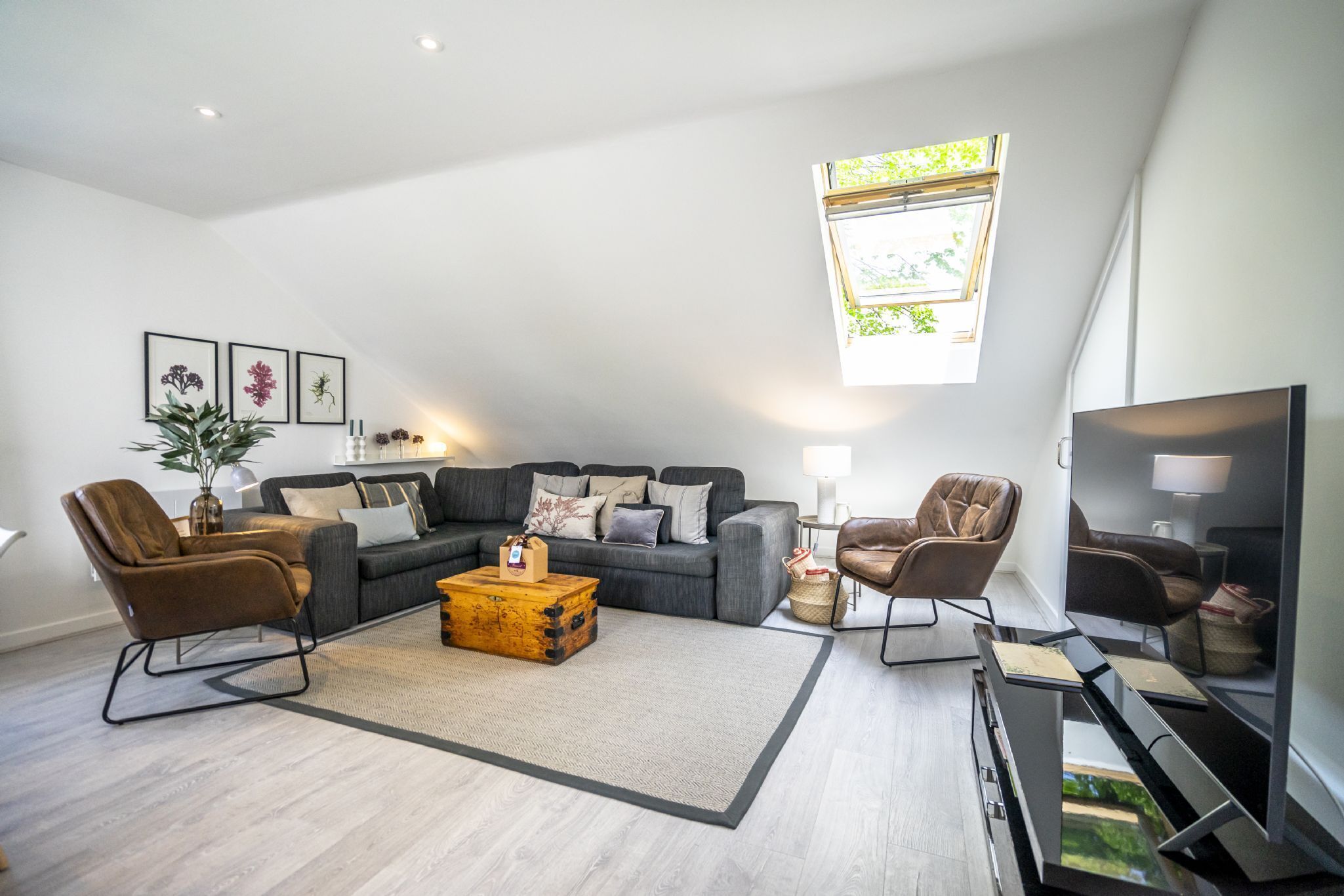 A modern living room with a sectional sofa, two armchairs, a coffee table, and a flat-screen TV.