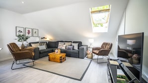 Una sala moderna con un sofá modular, dos sillones, una mesa de centro y un televisor de pantalla plana.