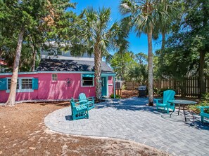 A pink house with turquoise accents, a paved patio with outdoor furniture, and a fenced yard with palm trees.