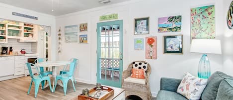 A bright, well-lit living area with a kitchen, a dining table with chairs, a sofa, and various wall decorations.