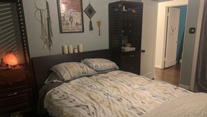 Ein Schlafzimmer mit einem Bett, einem Nachttisch, einer Wandlampe, einem gerahmten Bild und einem Kleiderschrank.
