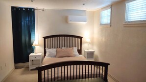 A bedroom with a bed, nightstands, a window with blinds, and an air conditioning unit.