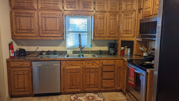 A kitchen with wooden cabinets, a stainless steel dishwasher, a sink, a coffee maker, and a stove.