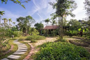 A garden with a winding stone path, various plants, and a structure with a red roof. - Thai Gia Trang Farmstay (Hue)