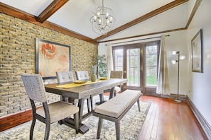 A dining area with a brick wall, wooden beams, a chandelier, and a view of the outdoors.