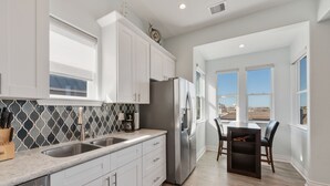 A modern kitchen with white cabinets, stainless steel appliances, and a large window overlooking a scenic view. - Family Friendly Beach House in Gated Beach Resort (Galveston)