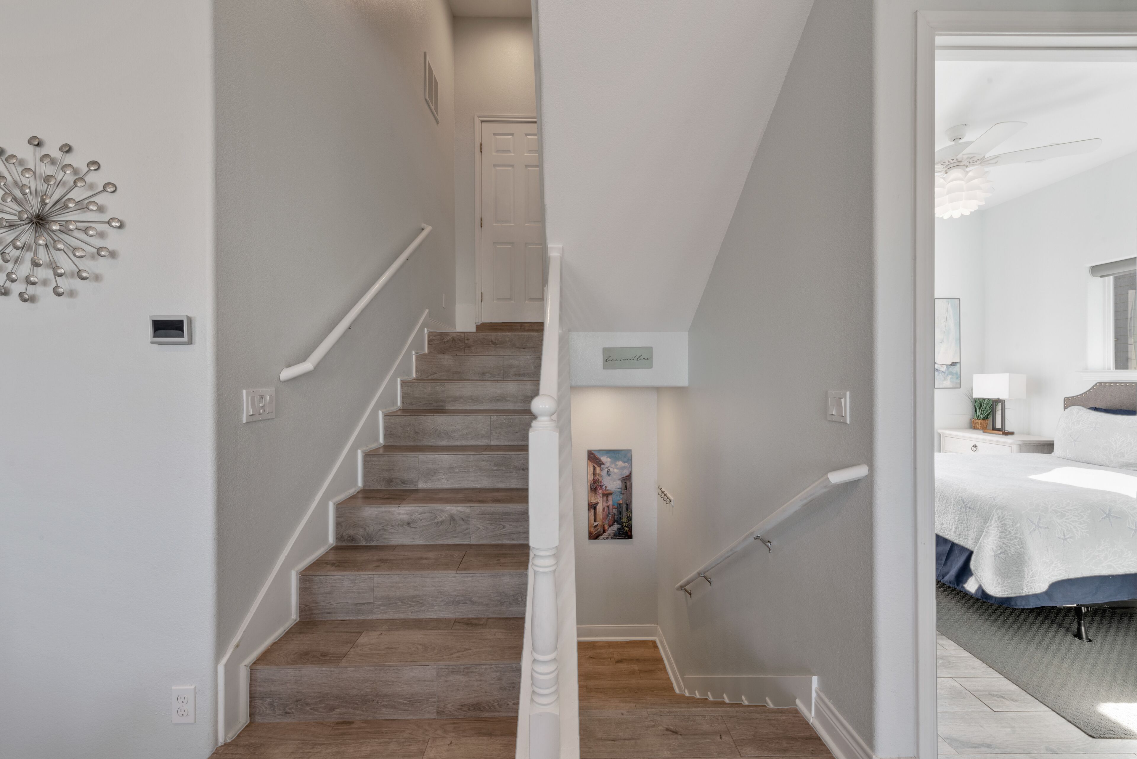 Una escalera de madera con barandillas blancas que conduce a un dormitorio con cama y mesita de noche.