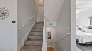 A staircase with wooden steps and white railings leading to a bedroom with a bed and a nightstand. - Family Friendly Beach House in Gated Beach Resort (Galveston)