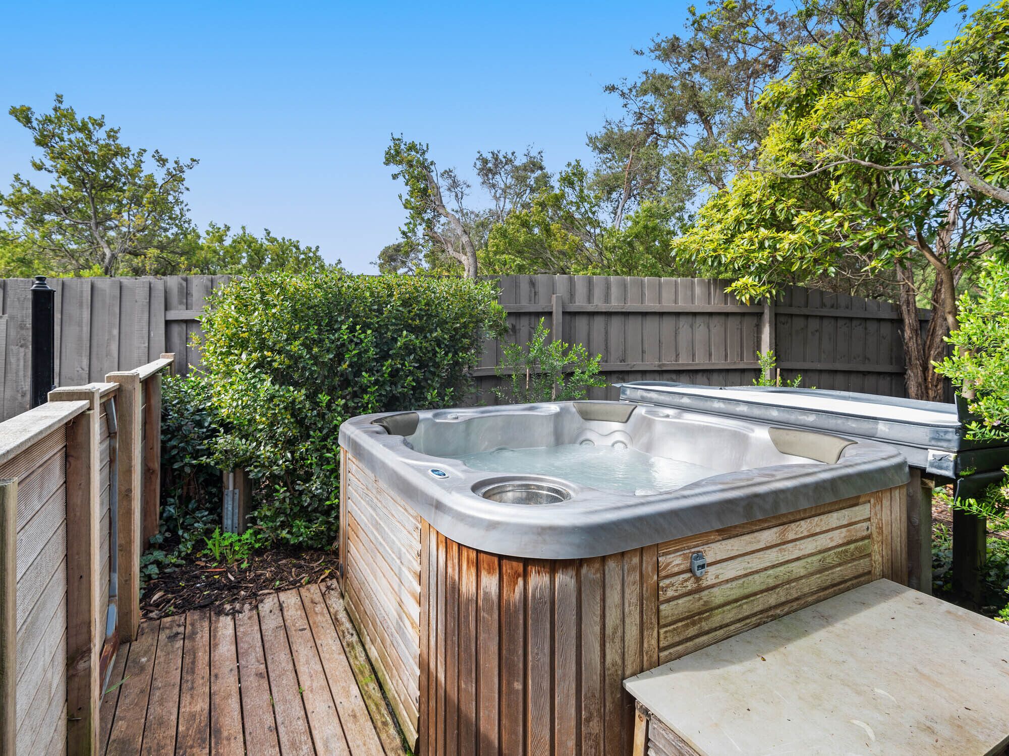 Un bain à remous dans un jardin, avec une terrasse en bois et une clôture en bois.