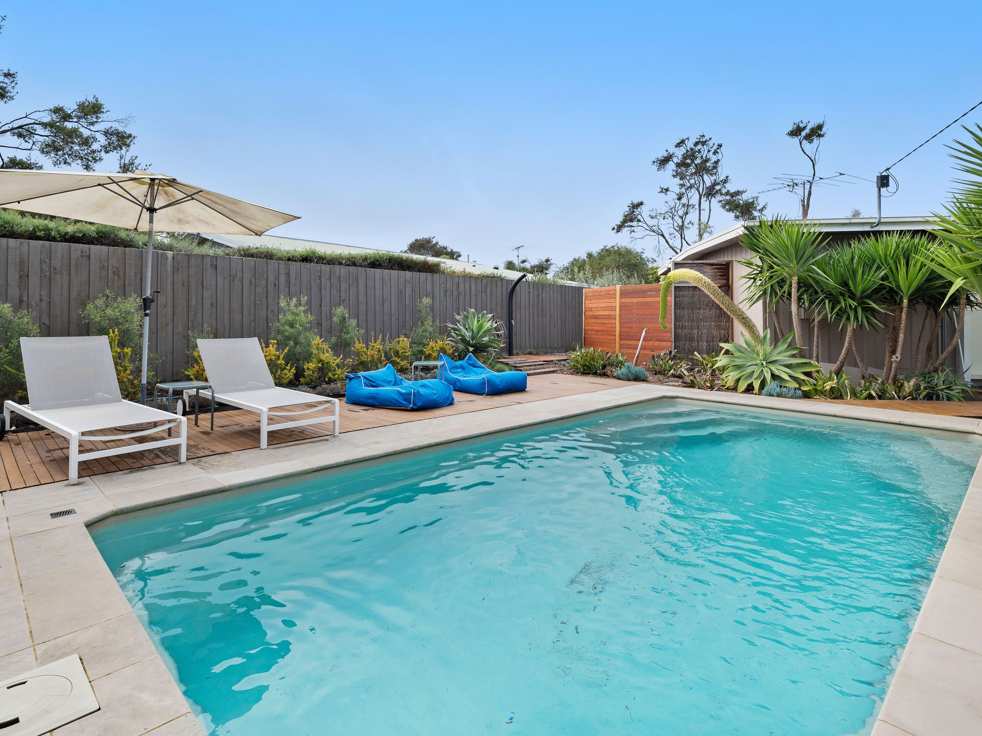 A backyard with a swimming pool, two white lounge chairs, and blue bean bags.