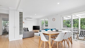 Ein modernes Wohnzimmer mit Essbereich, großen Fenstern und einem eingebauten Fernseher.