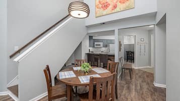 Een eetgedeelte met een houten tafel en stoelen, een trap, een keuken en een zithoek met een 'WELCOME' bord.