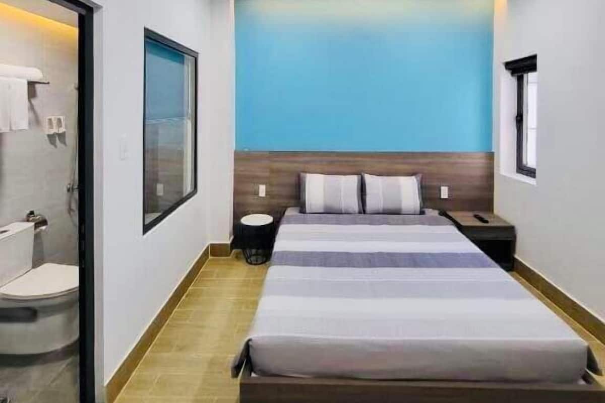 Un dormitorio moderno con una cama grande, un cabecero de madera, una mesita de noche pequeña y una ventana.