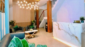 A modern reception area with a marble reception desk, a staircase, and a seating area with leather sofas and a coffee table.