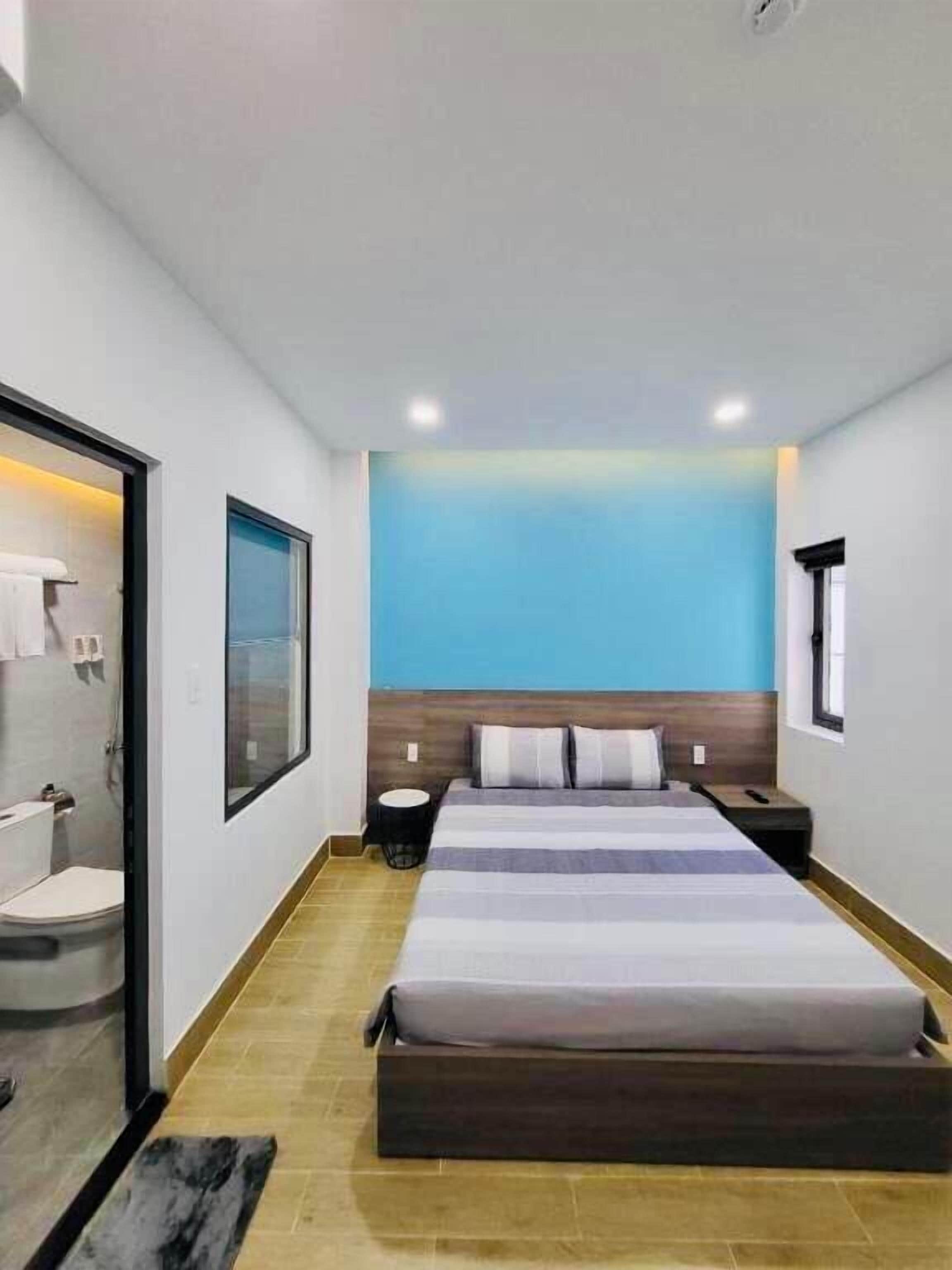 Een moderne slaapkamer met een groot bed, een houten hoofdbord, een klein nachtkastje en een raam.