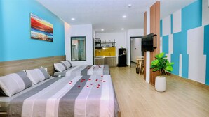 A modern hotel room with a bed, a TV, a small kitchen area, and a potted plant.