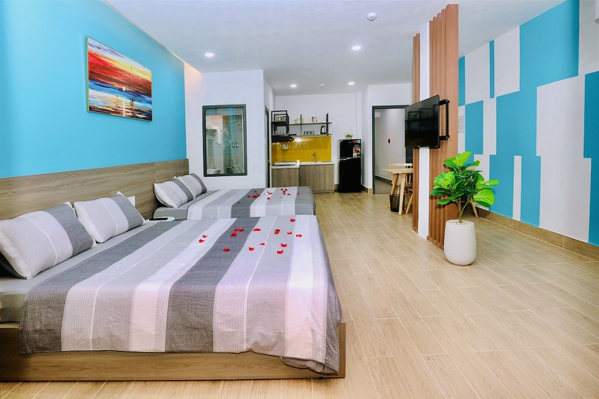 Una habitación de hotel moderna con una cama, un televisor, una pequeña cocina y una planta en maceta.