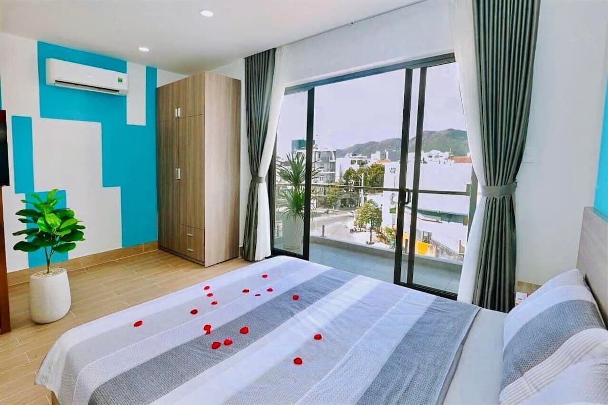 Habitación de hotel con una cama grande, una planta en maceta, un equipo de aire acondicionado y vistas a la ciudad.