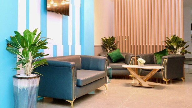 A modern reception area with a blue and white striped wall, a mounted television, a wooden slatted partition, and a hanging light fixture.