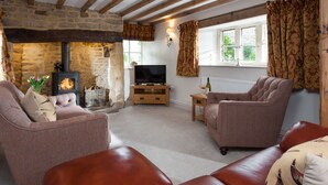 A cozy living room with a stone fireplace, comfortable seating, and a television. - The Nook - Guiting Power, Cheltenham sleeping 6 guests (Guiting Power)
