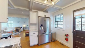 A modern kitchen with a stainless steel refrigerator, wooden flooring, and white cabinetry.